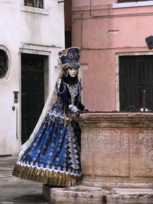 Eine Frau im für Venedig typischen Karnevalskostüm an einem Brunnen von Venedig