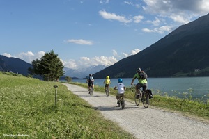 Eine Familie radelt auf dem Radweg der Via Claudia Augusta am Reschensee vorbei