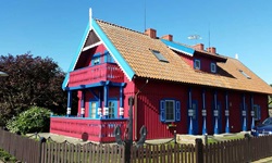 Ein auffällig rotes Holzhaus mit blau-weißen Fensterläden auf der kurischen Nehrung.