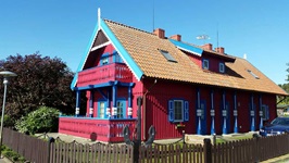 Ein auffällig rotes Holzhaus mit blau-weißen Fensterläden auf der kurischen Nehrung.