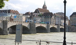 Stadtansicht von Basel mit der Mittleren Brücke ujnd dem Rathausturm. Im Bildvordergrund lehnt ein Fahrrad an der Begrenzung des Rheinufers.