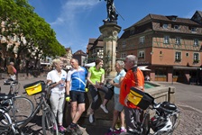 Eine Gruppe Radfahrer macht beim Schwendi-Brunnen in Colmar Pause.