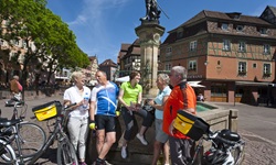 Eine Gruppe Radfahrer macht beim Schwendi-Brunnen in Colmar Pause.