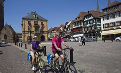Ein Radlerpärchen überquert den Marktplatz (Place du Marché) von Obernai.
