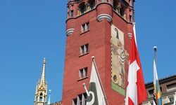 Verschiedene Fahnen vor dem aus rotem Stein erbauten Rathaus in Basel mit seinem charakteristischen Turm.