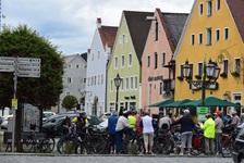 Eine Gruppe Fahrradfahrer macht Pause auf einem Gehweg, im Hintergrund ist eine Häuserreihe zu sehen