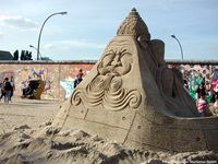 Blick auf eine Steinskulptur bis zu einem Teilabschnitt der Berliner Mauer