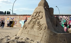 Blick auf eine Steinskulptur bis zu einem Teilabschnitt der Berliner Mauer