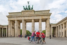 Drei Radler - zwei Frauen und ein Mann - sind vor dem Brandenburger Tor in ihre Reiseunterlagen vertieft.