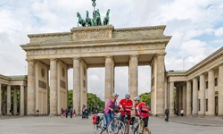 Drei Radler - zwei Frauen und ein Mann - sind vor dem Brandenburger Tor in ihre Reiseunterlagen vertieft.