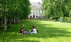 Drei junge Frauen und ein Kind sitzen vor der Liebermann-Villa in Berlin auf einer Wiese.