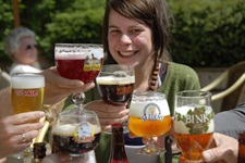 Eine junge Frau sitzt an einem Tisch und prostet mit anderen die verschiedensten Biere der Provinz Limburg zu