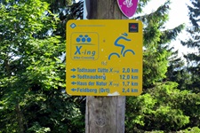 Ein typischer, gelber Wegweiser der Schwarzwald-Bike-Crossing-Strecke mit stilisiertem Schwarzwälder Bollenhut und Mountainbiker.