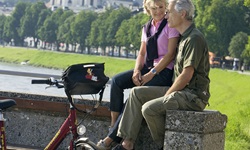 Ein Paar sitzt auf einer Mauer, im Vordergrund steht ein Fahrrad und im Hintergrund ist die Burg von Salzburg zu sehen