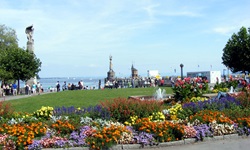 Parkanlage in Konstanz mit wunderschönen Blumenbeeten und einem Springbrunnen - im Hintergrund ist der Hafen mit der Imperia zu erkennen