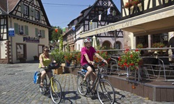 Zwei Fahrradfahrer fahren durch die französische Gemeinde Börsch an einem Café vorbei