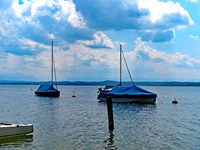 Zwei mit blauen Planen abgedeckte Boote dümpeln auf dem Starnberger See.