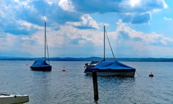 Zwei mit blauen Planen abgedeckte Boote dümpeln auf dem Starnberger See.