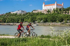 Zwei Radler fahren auf dem Donau-Radweg an der Burg von Bratislava vorbei.