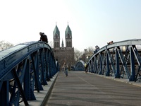 Fahrradfahrer überquert eine Brücke - im Hintergrund ist ein Dom mit zwei Türmen zu erkennen