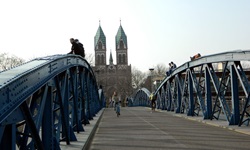 Fahrradfahrer überquert eine Brücke - im Hintergrund ist ein Dom mit zwei Türmen zu erkennen