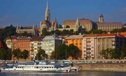 Die Budapester Innenstadt mit der Matthiaskirche und der Fischerbastei vom Burgberg aus gesehen. Im Bildvordergrund sind Schiffe auf der Donau zu sehen.