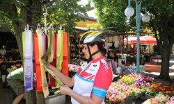 Eine Radlerin bummelt über einen ungarischen Markt und begutachtet die an einem Stand angebotenen bunten Schals.
