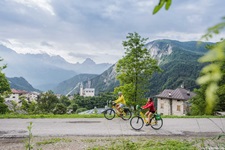 Zwei Radfaherer fahren auf dem Radweg von den Dolomiten nach Venedig an einem typischen Dorf der Dolomiten entlang