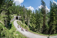 Vier Radfahrer auf dem Berg-Wald-Radweg von den Dolomiten nach Venedig, hinter ihnen ein Tunnel durch den Berg