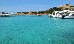 Mehrere Boote liegen bei der Insel Caprera im kristallklaren Wasser.