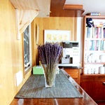 Detailansicht des Restaurants auf der Caprice: Eine Vase mit Lavendel steht auf einem Sideboard, im Hintergrund sind die Cafémaschine und das Bücherregal zu erkennen
