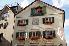Blick auf ein Gästehaus mit roten Blumen geschmückten Fenstern und einer Wandmalerei mit zwei Gänse in Chur