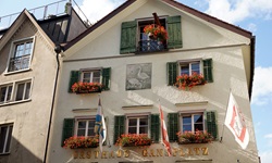 Blick auf ein Gästehaus mit roten Blumen geschmückten Fenstern und einer Wandmalerei mit zwei Gänse in Chur