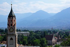 Der markante Turm der Pfarrkirche St. Nikolaus in Meran erhebt sich vor einer beeindruckenden Bergkulisse.