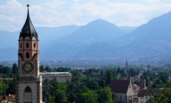 Der markante Turm der Pfarrkirche St. Nikolaus in Meran erhebt sich vor einer beeindruckenden Bergkulisse.