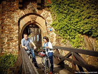 Ein Radfahrerpärchen steht auf der Brücke von Burg Thurgant und liest eine Infobroschüre.
