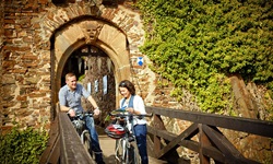 Ein Radfahrerpärchen steht auf der Brücke von Burg Thurgant und liest eine Infobroschüre.