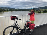 Eine Radfahrerin steht neben ihrem Fahrrad am Geländer einer Brücke über die Donau