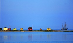 Ein Segelschiff liegt neben bunten Häuschen, wie sie für viele Inseln der Dänischen Südsee typisch sind, vor Anker.
