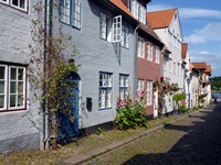 Schöner Blick in eine verträumte kleine Gasse mit blühenden Stockrosen und bunten Hausfassaden.