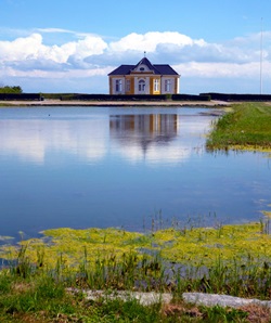 Ein in gelb und weiß gehaltenes HÄuschen steht idyllisch am Ufer eines Sees.