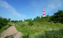 Ein Sandweg zu einem rot-weiß gestreiften Leuchtturm auf der Insel Ameland