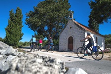 Sechs Radler passieren die an der Straße von Srednje Selo nach Grohote gelegene Kapelle des Heiligen Michael auf der Insel Šolta.
