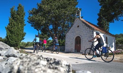 Sechs Radler passieren die an der Straße von Srednje Selo nach Grohote gelegene Kapelle des Heiligen Michael auf der Insel Šolta.