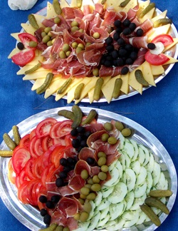 Platten mit Essen: Käse, Gewürzgurken, Oliven, Schinken, Gemüsegurken und Tomaten