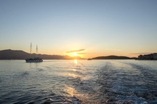Ein Motorsegler mit zwei Masten verlässt im beginnenden Sonnenuntergang einen Hafen in Süddalmatien.