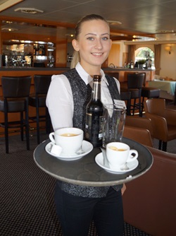 Eine Kellnerin der MS De Willemstad mit einem voll beladenen Tablett, afu dem Kaffee und eine Bierflasche stehen.