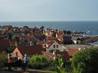 Eine Gruppe Menschen sitzt auf einer Bank und blickt über die Dächer eines Dorfes zum Meer auf der Insel Bornholm