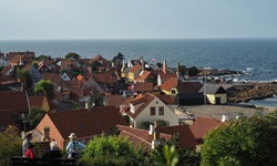 Eine Gruppe Menschen sitzt auf einer Bank und blickt über die Dächer eines Dorfes zum Meer auf der Insel Bornholm