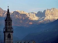 Der Turm des Bozener Doms vor der Kulisse der Bozen umrahmenden Dolomitengipfel.